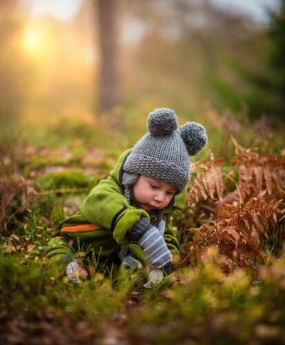 chłopiec siedzi na ziemi w lesie i szuka czegoś w trawie
